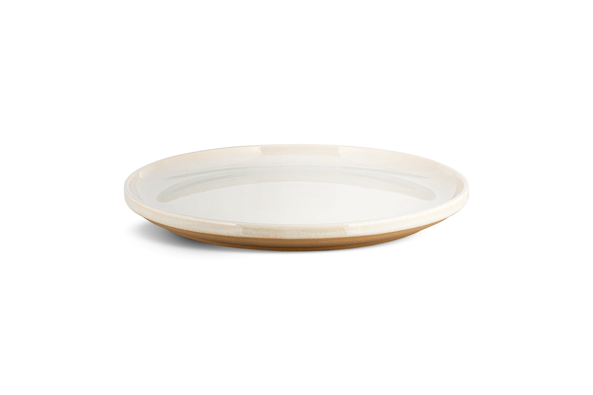 The Edo Dinnerware Set - Terracotta by nkuku features 12 minimalist, round ceramic plates with glossy white interiors and matte tan rims and bases. The design's earthy tones and lack of decoration create a serene, stylish tabletop look.