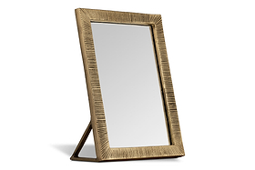 The nkuku Baja Standing Mirror - Antique Brass features a rectangular design with a gold textured frame and vertical grooves. Supported by a triangular stand, it has a modern, elegant look with a metallic matte finish.