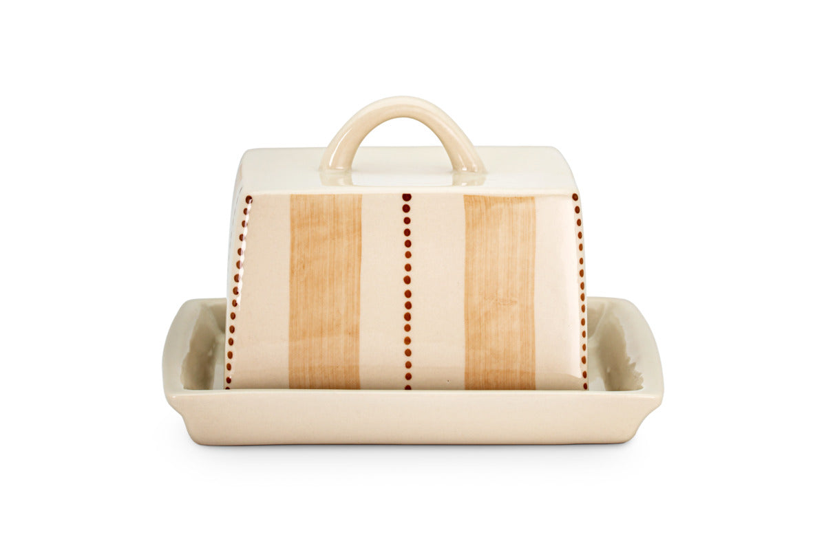 The Patthar Butter Dish - Cream & Clay by nkuku is hand-painted with vertical beige stripes and dotted accents. It features a curved handle, a fitted lid, and sits on a matching cream tray. Shown on a plain white background.