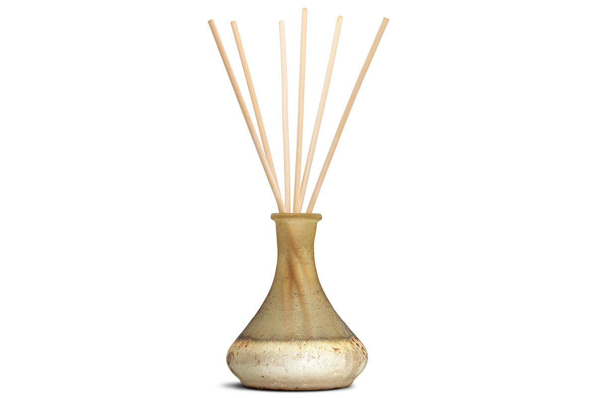 A yellow Oakmoss & Rose Scented Reed Diffuser by nkuku features several tall, slender natural-colored reed sticks fanned out from the top. The hand-blown glass vessel has a narrow neck and rounded base, showcasing a subtly textured, rustic finish that enhances its delicate floral fragrance.