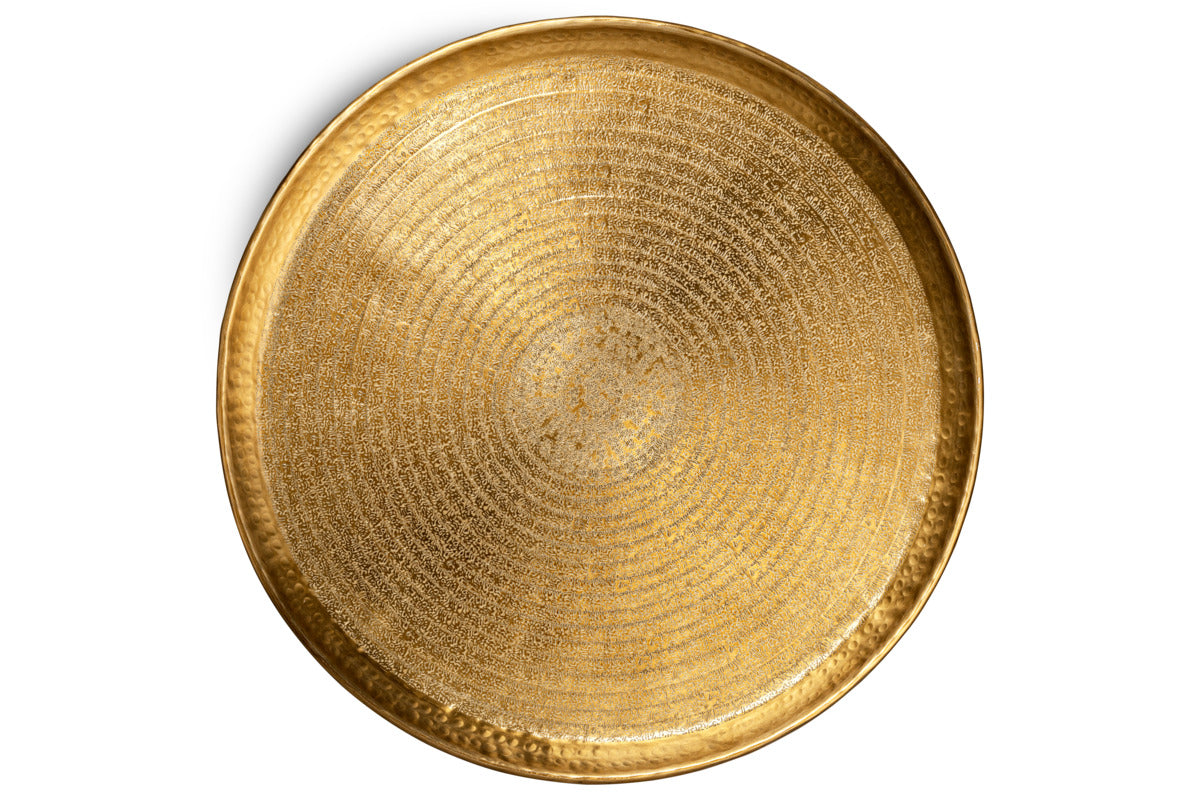 The Amai Etched Round Tray by nkuku is shown from above. Crafted in brass, this decorative serving tray features a gently raised edge and an intricately textured surface with circular patterns, creating a shimmering, eye-catching effect. Set against a plain white background, the tray’s detailed gold design stands out beautifully.