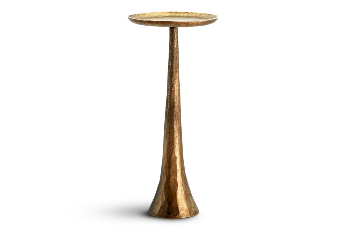 The Lora Pillar Candle Holder - Brass by nkuku is a tall, metallic pedestal crafted in gold with a hammered texture, featuring a slender, tapered stem and a wide, shallow round top. This sculptural candle holder makes an elegant table centerpiece and is shown against a plain white background.