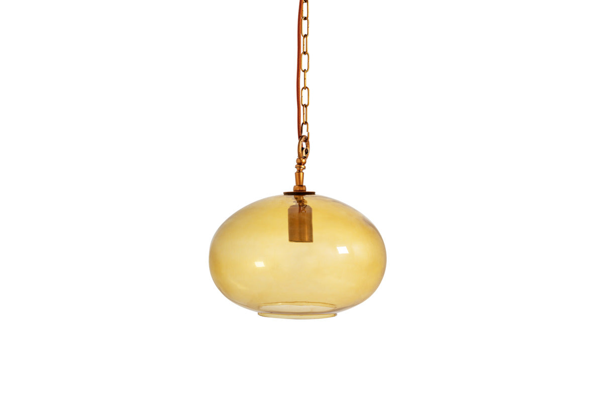 The Otoro Recycled Glass Pendant - Honey - Small Round by nkuku features a smooth, translucent amber-toned globe crafted from recycled glass, suspended from a coordinating coppery brown chain and cord. Subtle brass fittings accentuate its minimalist, modern design while the visible bulb socket within adds an industrial touch.