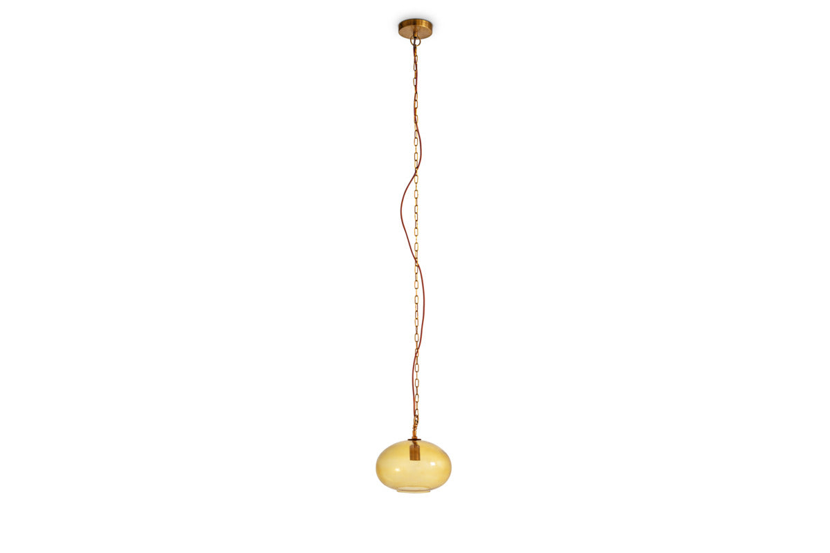 A gold chain and exposed cord suspend nkuku’s Otoro Recycled Glass Pendant - Honey - Small Round from the ceiling, showcasing its round amber glass shade with sleek brass fittings. Set against a plain white background, the pendant’s simple, modern design and eco-friendly recycled glass construction stand out.
