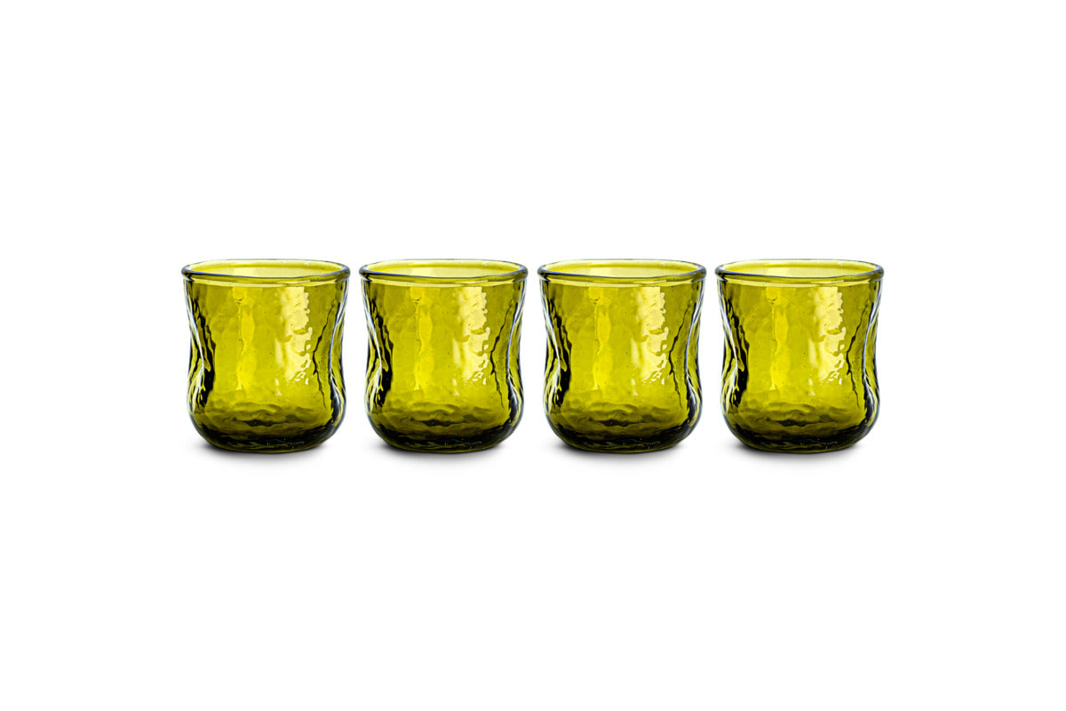 A set of four nkuku Chandani Tumbler - Green - Short glasses, each featuring a subtly tapered shape and textured hammered surface, are arranged in a row on a white background. This handmade glassware boasts a modern design with a translucent finish.