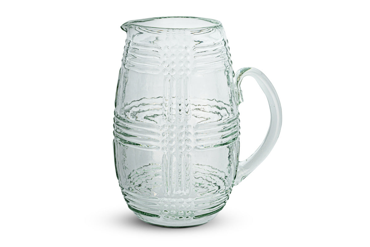 The nkuku Kaanch Jug – Clear features a wide-bodied design with a sturdy handle and is crafted from clear glass. Its body showcases an embossed check pattern composed of raised dots and lines, while a small spout adds to its functional charm. The jug is displayed on a plain white background.