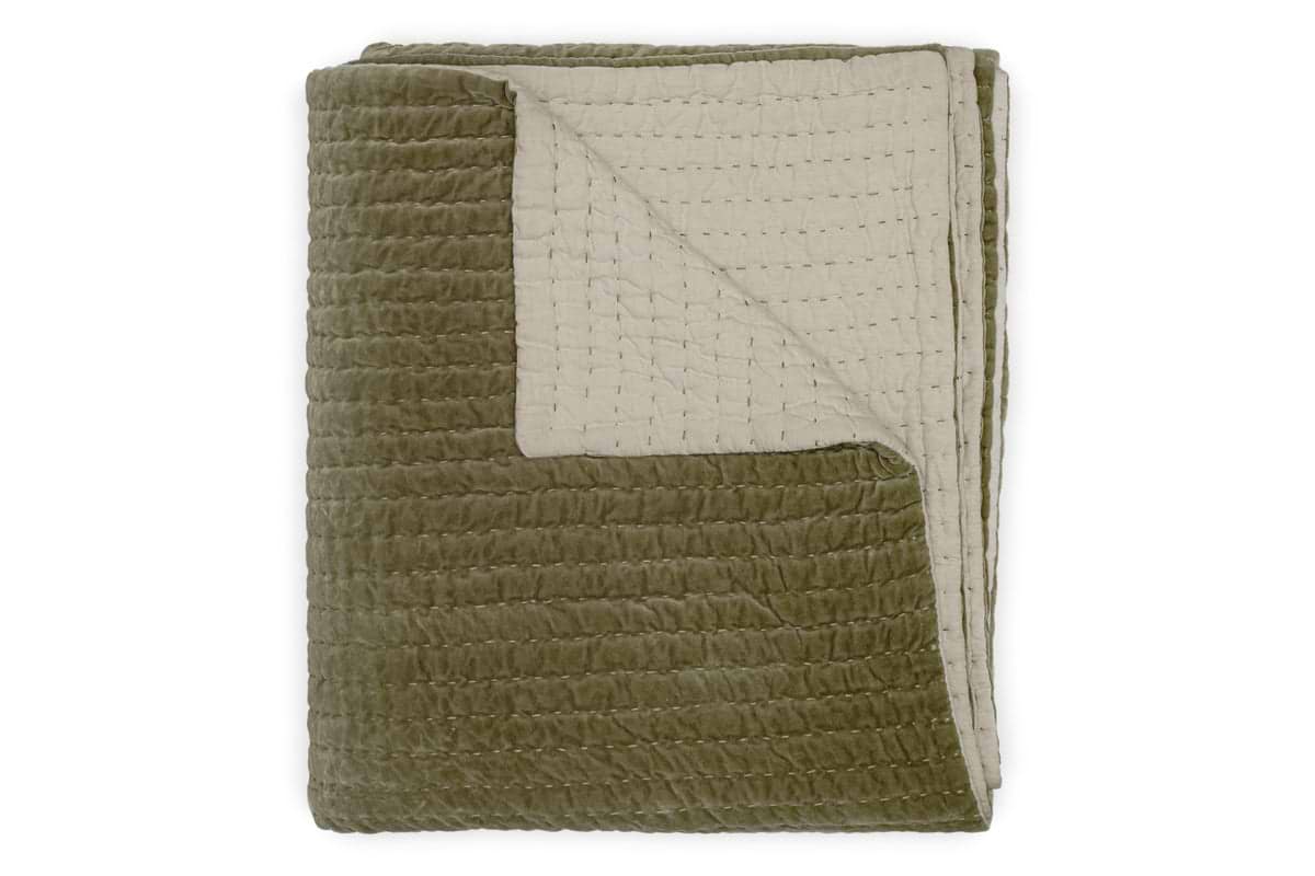 The nkuku Nidra Velvet & Linen Bed Quilt in Moss features a folded olive green velvet top, light beige linen underside, Kantha quilting, and intricate stitching, with one corner flipped to display both colors and detailed craftsmanship.