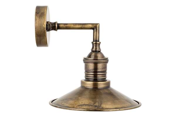 The Najja Brass Wall Lamp by nkuku features an angled arm and wide conical shade with an antique brass finish, adding vintage charm. This classic wall sconce mounts easily on a round plate for effortless installation.