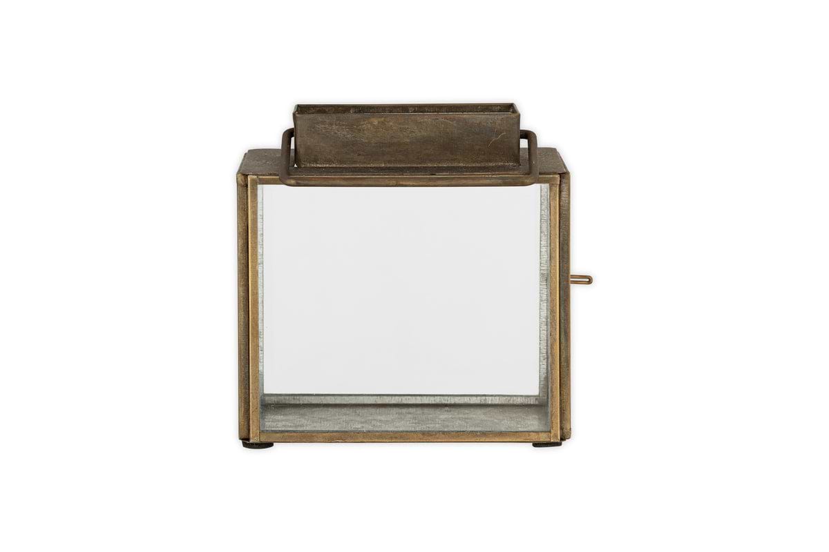 The Obi Mini Table Lantern by nkuku features an antique brass square frame, glass sides, a rectangular handle on top, and a glass door for easy access, shown against a plain white background.