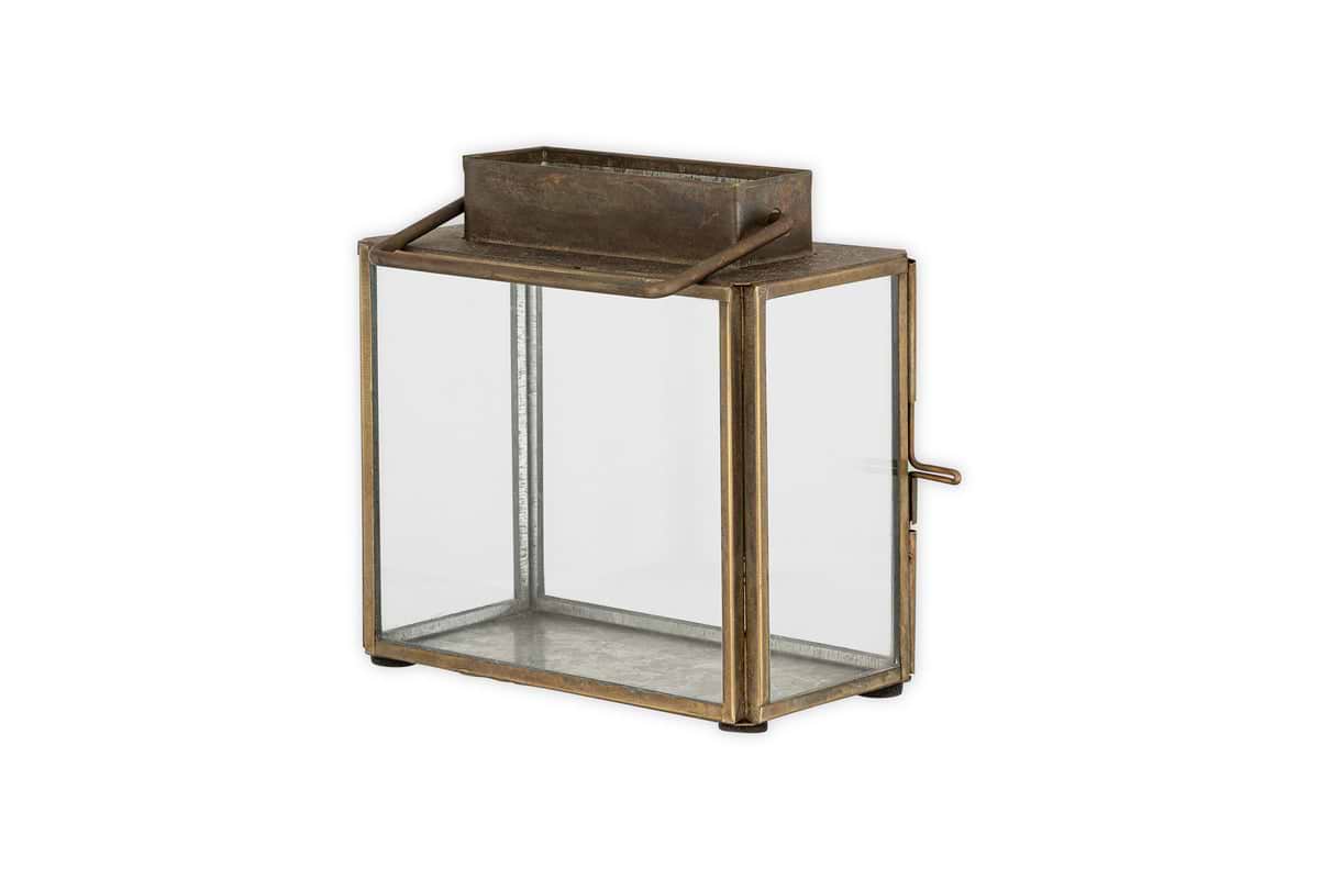 The Obi Mini Table Lantern by nkuku features an antique brass finish, a glass door, and handle—perfect for soft candlelight or as a charming decorative accent.