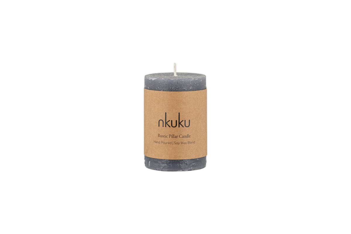 The Rustic Soy Blend Mini Pillar Candle - Charcoal by nkuku is a grey mini pillar candle with a textured finish and a brown label, shown against a white background.