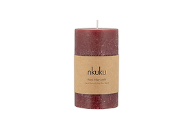 A small nkuku Rustic Soy Blend Pillar Candle in Dark Cherry with a textured finish and a brown paper label stands upright on a white background.