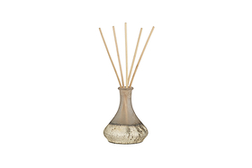 The nkuku Cardamom & Amber Reed Diffuser features a metallic-finished glass bottle filled with cardamom and amber fragrance and includes slim reeds to disperse scent. The product is set against a plain white background.