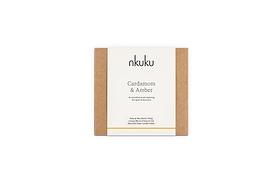 A rectangular box with brown sides and a white label reading “nkuku Cardamom & Amber 3 Wick Scented Candle,” a natural wax blend with sandalwood notes in a recyclable glass holder.