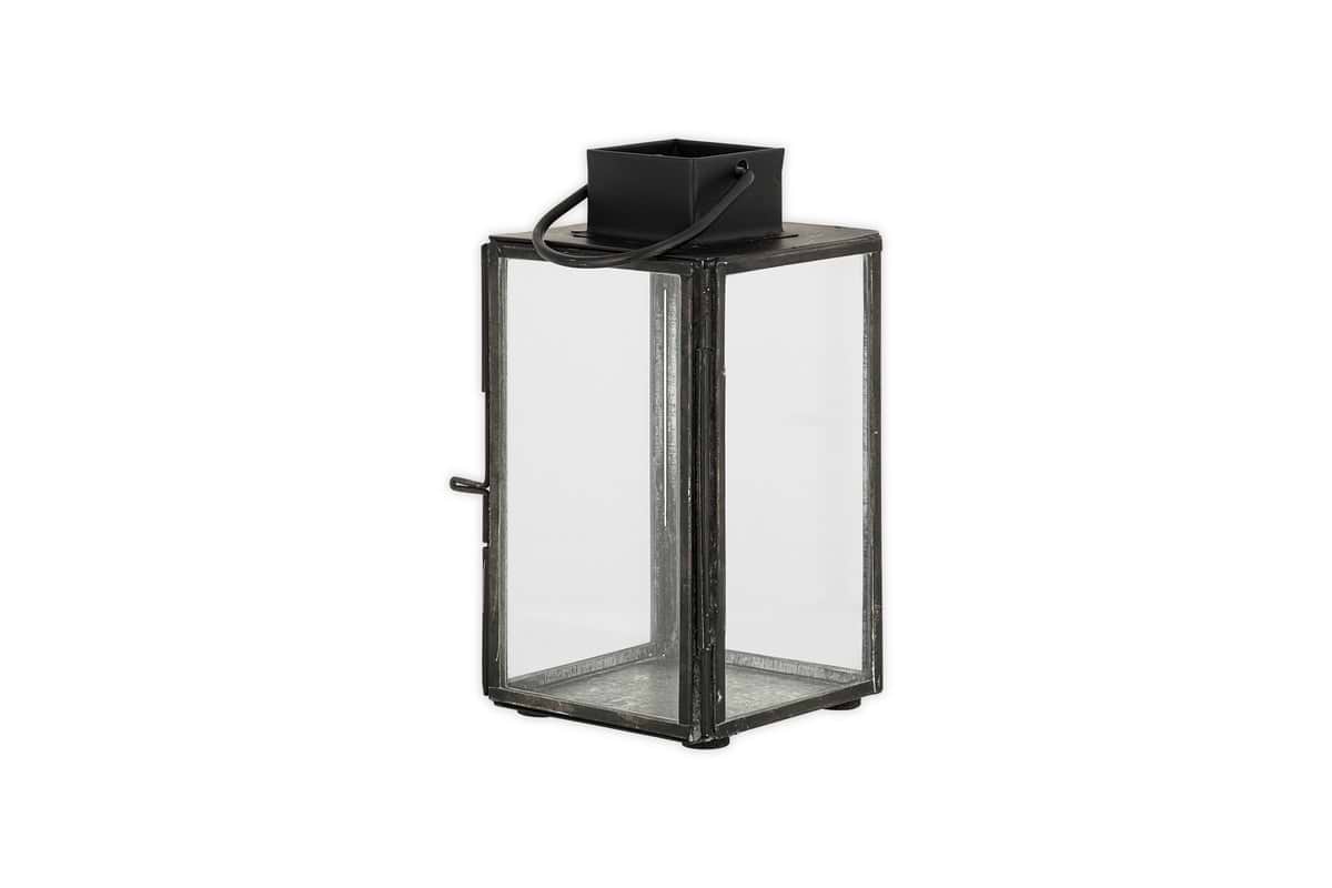 The nkuku Sia Mini Table Lantern - Black features clear glass panels, a top handle, and a hinged door for a tealight. Its rectangular metal frame stands on four small feet, adding charm to any setting.