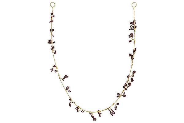 The nkuku Tanu Mango Wood Beaded Garland features brass and ruby beads, artfully clustered along the strand for a whimsical, foliage-inspired look. Displayed in a gentle U shape against a plain white background.