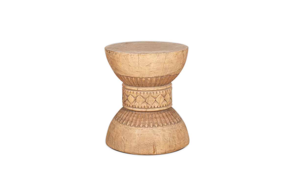 The Taru Carved Side Table - Natural by nkuku features a hand-carved, drum-shaped hourglass design with geometric patterns and textured details, showcasing Indian craftsmanship on a white background.