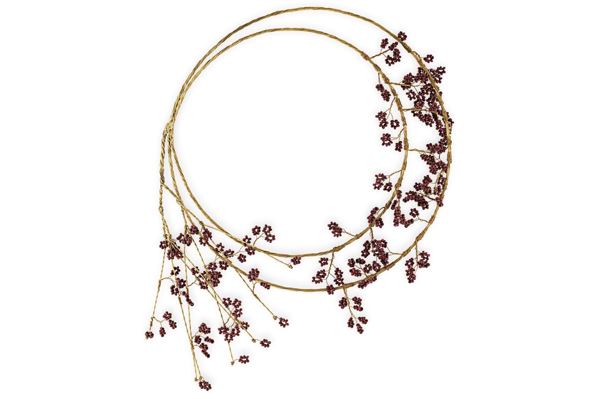 The Tanu Layered Mango Wood Beaded Wreath by nkuku features two intertwined brass-finished branches with clusters of ruby-red beads, arranged for a natural, asymmetrical look—a festive centerpiece for any space.