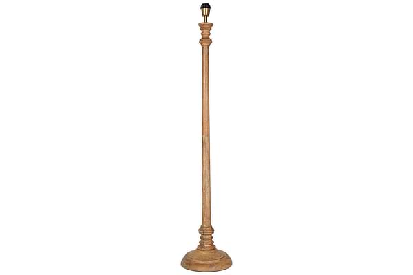 The Usha Classic Wooden Floor Lamp - Natural by nkuku is a tall, handmade mango wood base with a natural finish, round sturdy bottom, and ornately carved slender pole. Eco-friendly, it comes without a lampshade or bulb. Background is white.