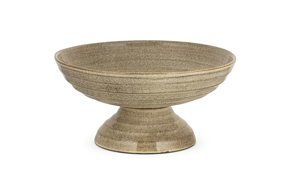 The Valinha Earthenware Footed Bowl by nkuku features a wide, shallow grey dish with a flared base and reactive glaze, ideal for enhancing rustic tablescapes. Displayed on a white background.