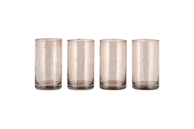 A set of four Yala Hammered Highball glasses by nkuku, made from recycled glass in a dusty terracotta hue, are arranged in a row on a white background.