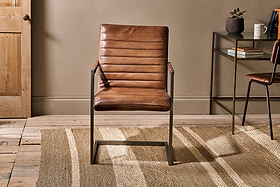The Wamma Leather Desk Chair by nkuku, featuring distressed dark brown leather and a ribbed design, sits on a jute rug in front of a tan wall.
