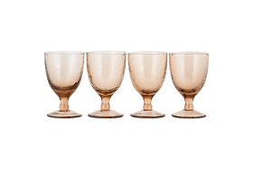 The nkuku Yala Hammered Wine Glass Set in Dusty Terracotta features four short-stemmed, amber-toned goblets with a subtle hammered pattern, round base, and slightly flared rim, arranged on a white background.