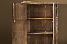 The Yasha Reeded Mango Wood Cabinet by nkuku stands against a plain brown wall with open doors, revealing two shelves. Its natural finish and visible grain create a rustic look, highlighting the cabinet’s well-crafted, empty interior.