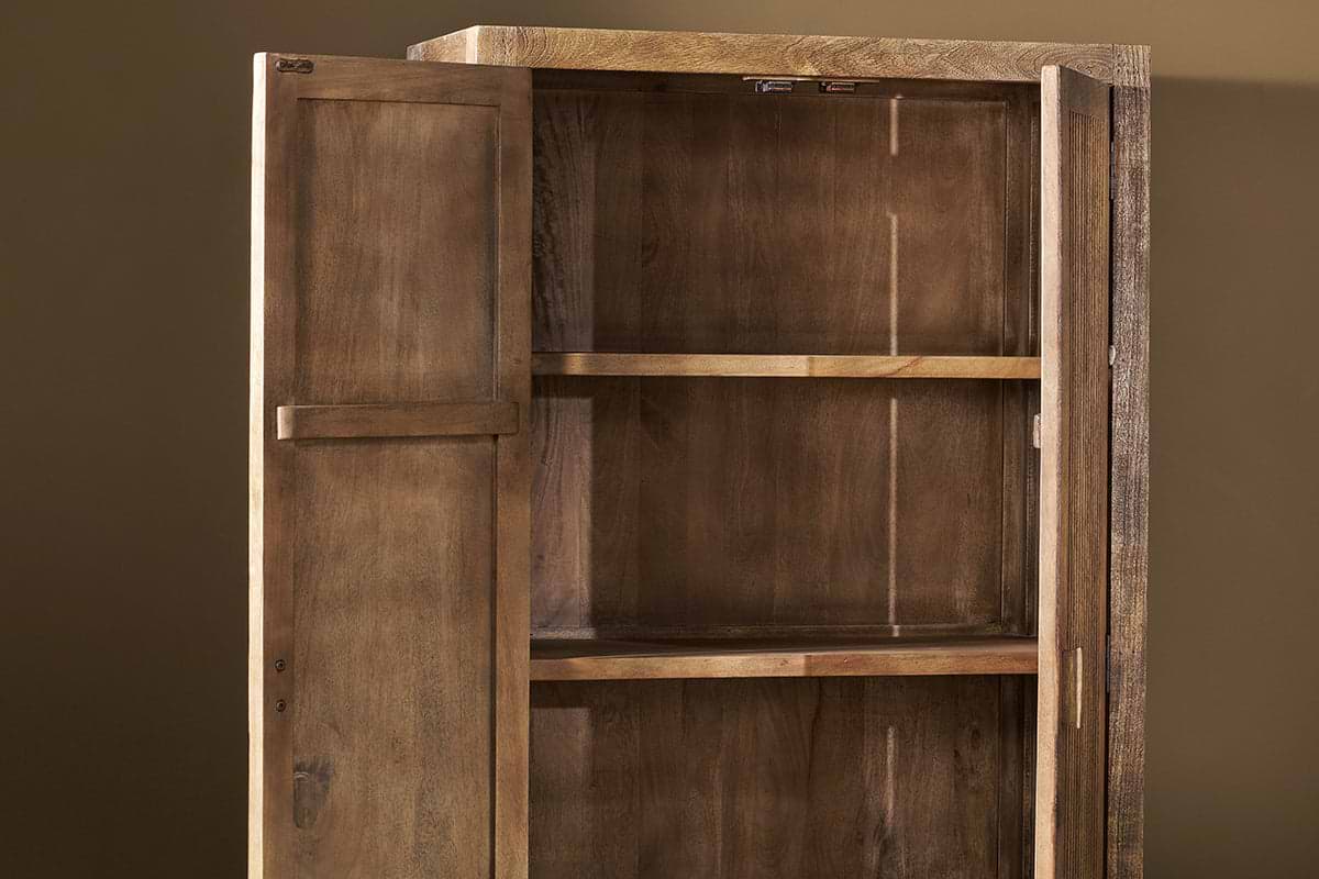 The Yasha Reeded Mango Wood Cabinet by nkuku stands against a plain brown wall with open doors, revealing two shelves. Its natural finish and visible grain create a rustic look, highlighting the cabinet’s well-crafted, empty interior.