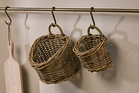 The Zawar Rattan Hanging Baskets - Natural (Set of 2) by nkuku hang from metal hooks on a rod, alongside a wooden paddle, creating a rustic and practical pantry storage display against a light-colored wall.