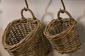 The nkuku Zawar Rattan Hanging Baskets - Natural (Set of 2) feature sturdy handles and a rustic, handcrafted look. These different-sized baskets are ideal for stylish pantry storage and hang easily from metal hooks on any wall.