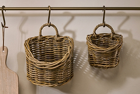 Two Zawar Rattan Hanging Baskets - Natural (Set of 2) by nkuku hang from a brass rod on the wall for chic pantry storage, while a wooden cutting board is displayed to the left.