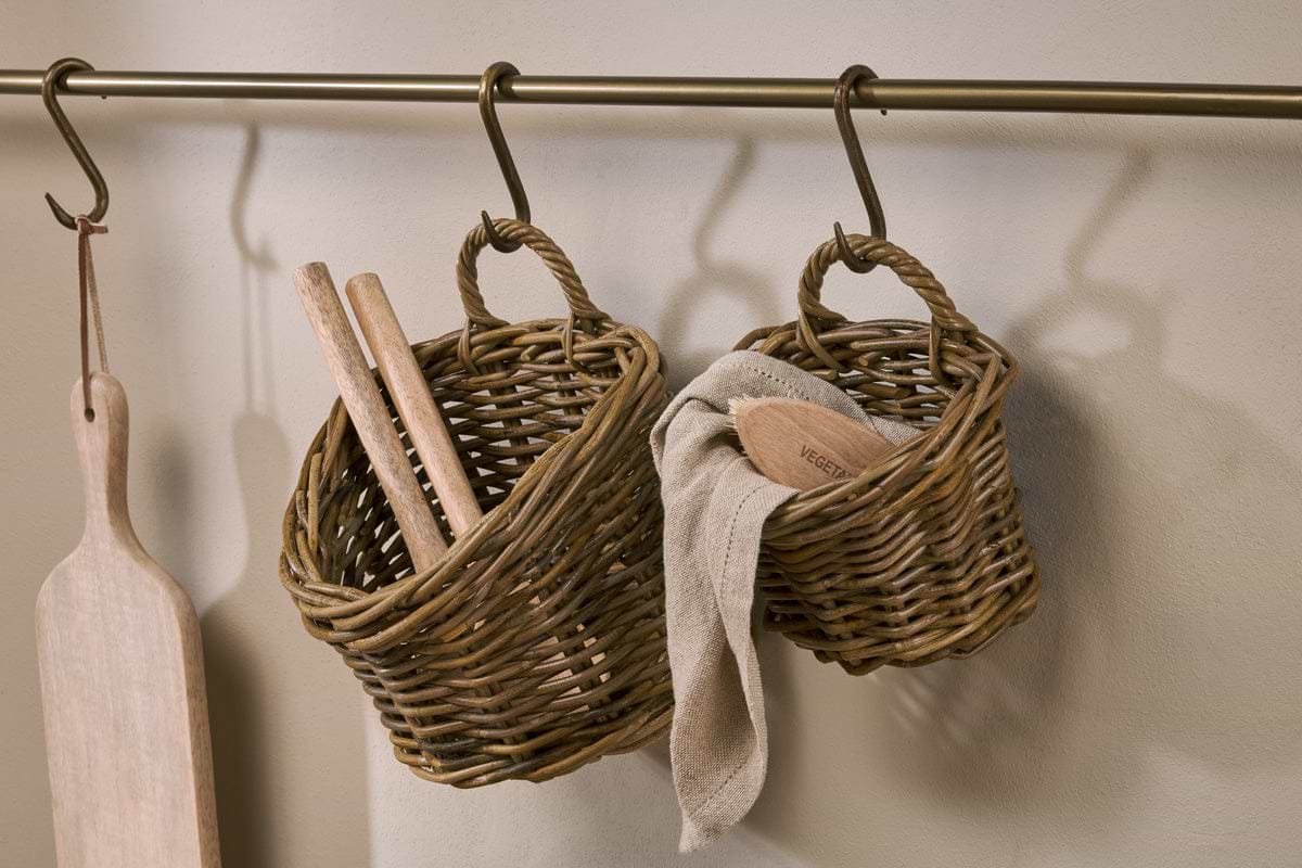 Nkuku’s Zawar Rattan Hanging Baskets – Natural (Set of 2) hang from an antique brass rail: one stores wooden utensils, the other provides handy pantry storage for a cloth and a brush labeled VEGETABLE.
