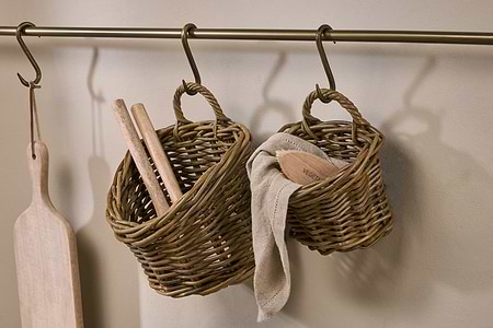 Nkuku’s Zawar Rattan Hanging Baskets – Natural (Set of 2) hang from an antique brass rail: one stores wooden utensils, the other provides handy pantry storage for a cloth and a brush labeled VEGETABLE.