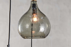 A close-up of the nkuku Ziva Recycled Glass Cluster Pendant in Green Smoke, featuring a clear, subtly smoky textured shade and glowing bulb—an adjustable modern pendant that stands out against a neutral background.