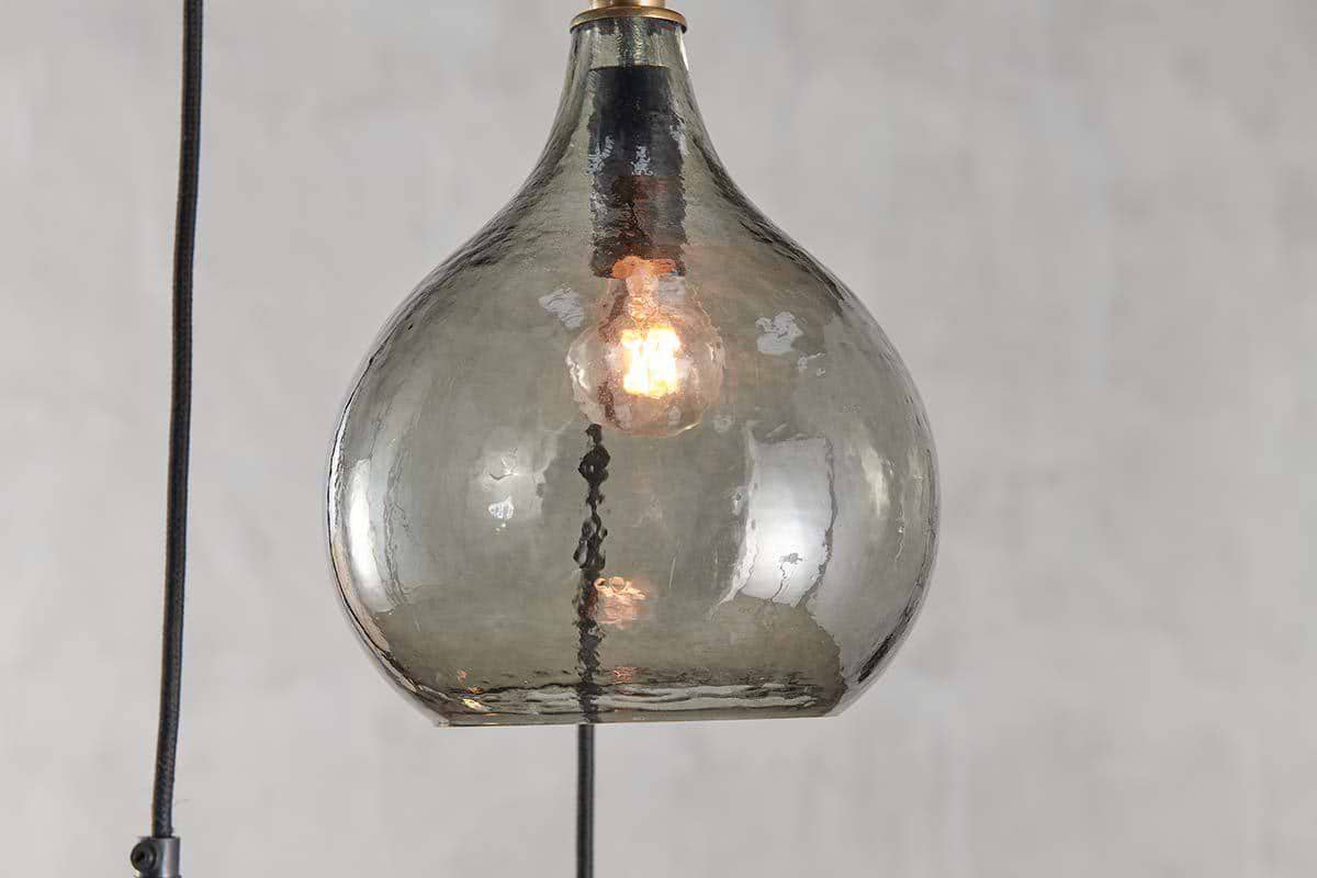 A close-up of the nkuku Ziva Recycled Glass Cluster Pendant in Green Smoke, featuring a clear, subtly smoky textured shade and glowing bulb—an adjustable modern pendant that stands out against a neutral background.