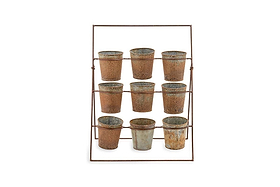 The Abari Planter Stand by nkuku holds nine rustic aged zinc pots in three rows. Angled backward for display, this minimalist metal rack showcases weathered pots—ideal as unique garden decor—against a plain white background.