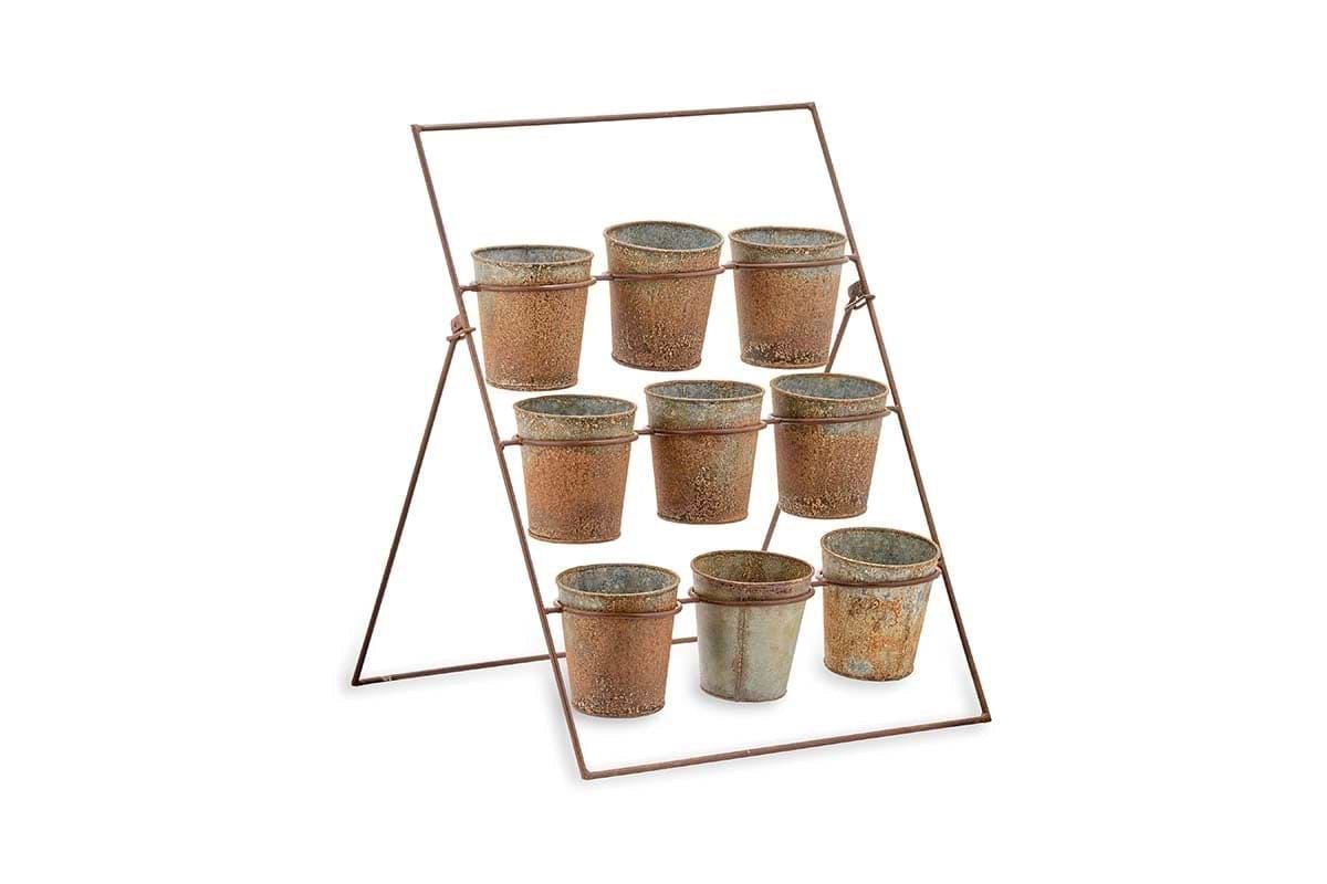 The nkuku Abari Planter Stand features three metal bars holding nine small, aged zinc pots with handles and unique patinas, arranged in a grid to create distinctive garden decor against a plain white background.