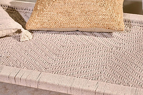 Close-up of the Kutumba Mango Day Bed by nkuku, featuring a handwoven jute chevron seat in beige, styled with a tan textured pillow and a smaller tassel pillow for a cozy, natural look.
