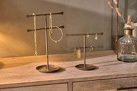 Two nkuku Liman Jewellery Stands with horizontal bars display gold jewellery on a light wooden dresser. Nearby, a glass vase with dried grasses sits against a beige wall, creating a warm, minimalist look.