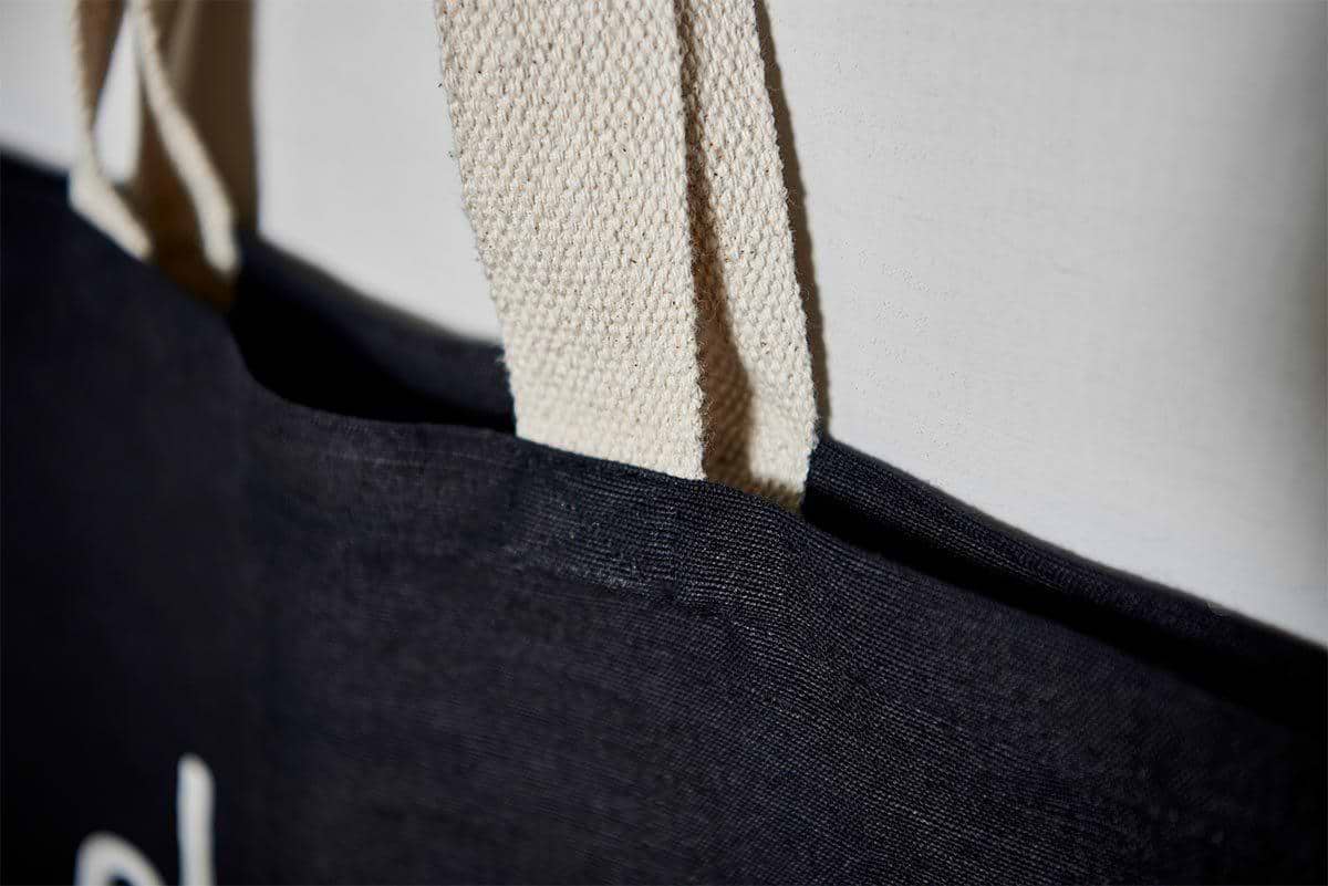 A close-up of nkuku's Jute & Cotton Tote Bag shows its black fabric and thick, textured beige handles stitched to the top edge—highlighting quality craftsmanship and a stylish choice for shopping.