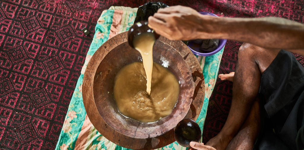 Person using a wooden mortar and pestle to grind a substance on a patterned fabric background