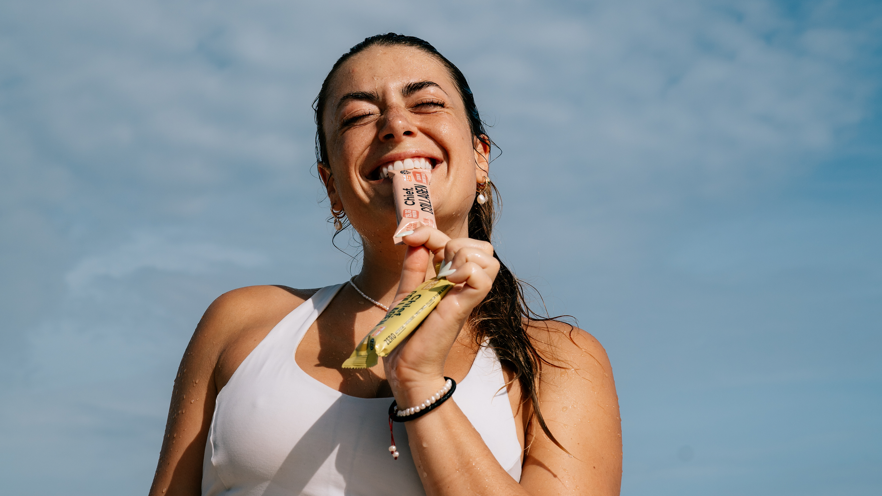 Woman holding a chief collagen bar against a blue sky
