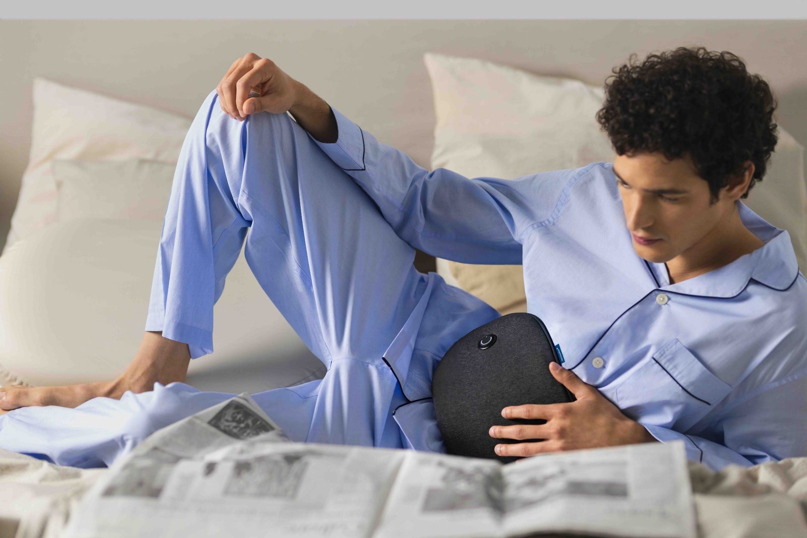 man on bed reading a newspaper with a cordless heating pad around his waist