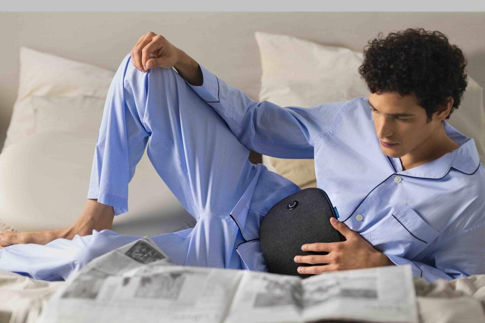 man on bed reading a newspaper with a cordless heating pad around his waist