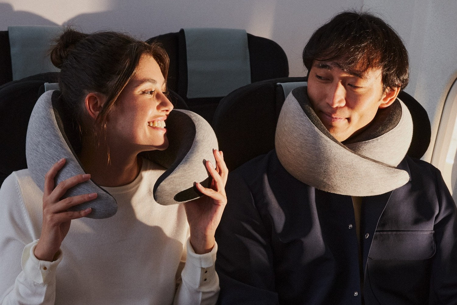 Woman adjusting Go Neck Pillow beside a man wearing one in an airplane seat.