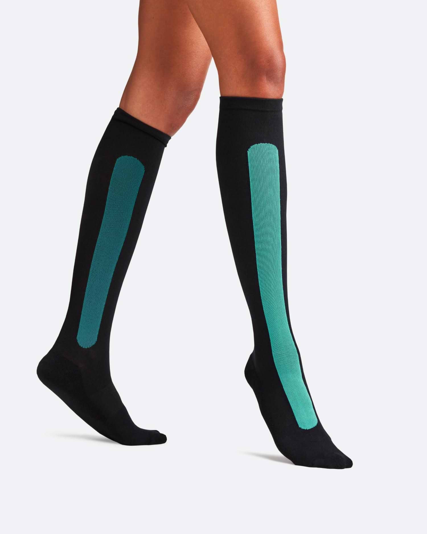 Side-profile view of a person walking, wearing knee-high Bamboo Compression Socks in the black and teal Blue Reef Caribbean Green colorway.