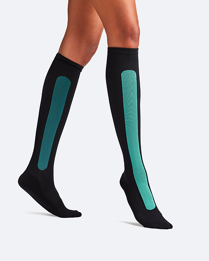 Side-profile view of a person walking, wearing knee-high Bamboo Compression Socks in the black and teal Blue Reef Caribbean Green colorway.