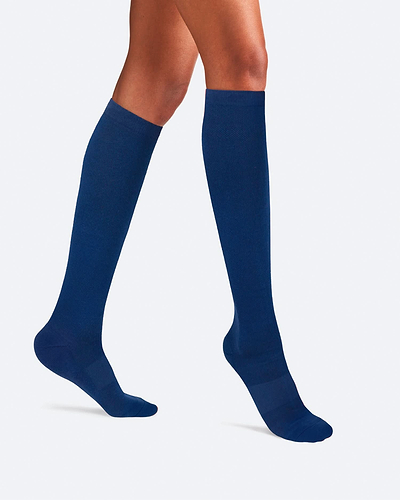 Side-profile view of a person's legs walking, wearing knee-high Ostrichpillow Bamboo Compression Socks in solid Seaside Siesta deep navy blue.
