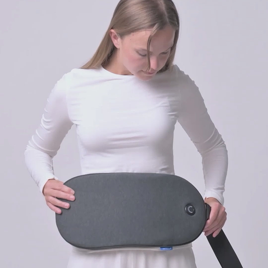 A woman presses the built-in circular power button to activate the warming pad on her Embrace Heating Pad, then positions it in her lumbar spine.